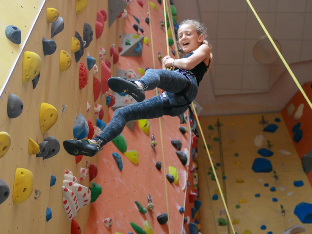 Person klettert lachend an der Kletterwand.